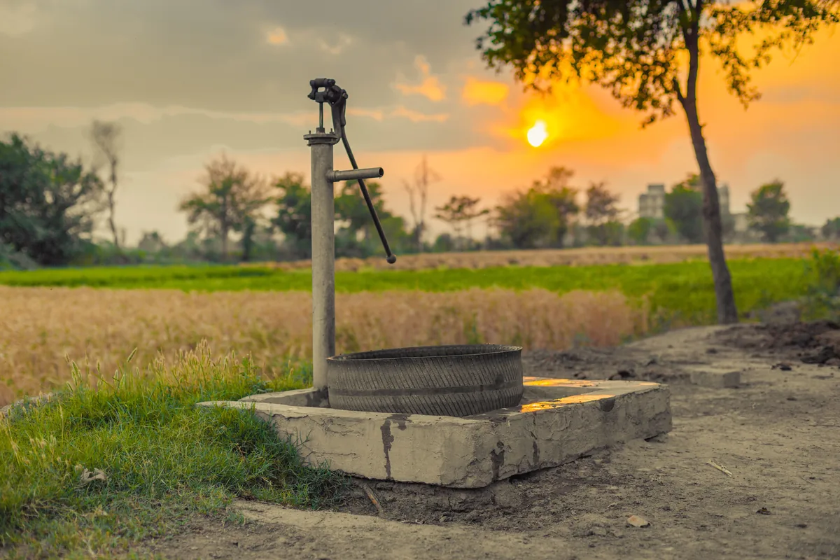 A cast iron hand water pump on a concrete well base in a farm field at dusk